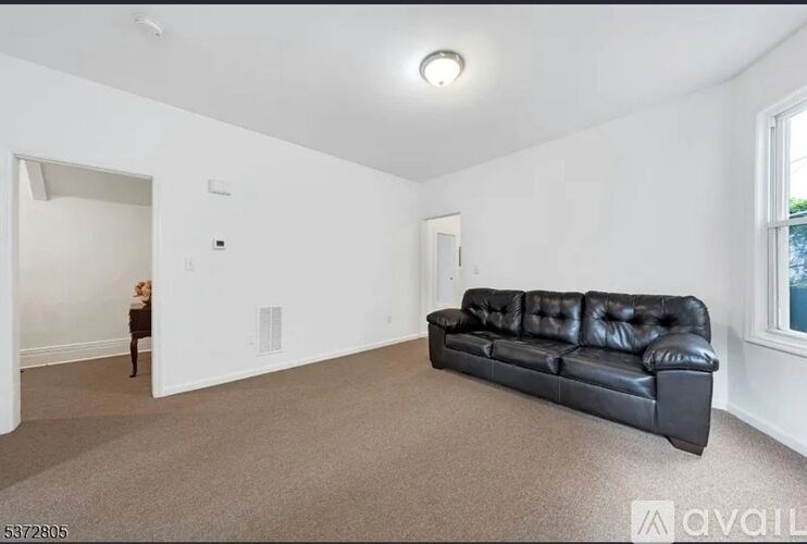 A woman stands in a spacious living room with a black leather couch.