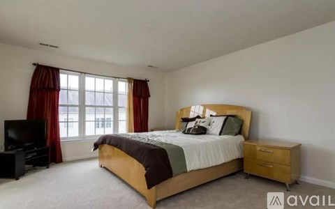 A bedroom with a large bed, a television, and a window with red curtains.