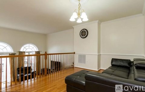 A living room with a black leather couch and a wooden floor.