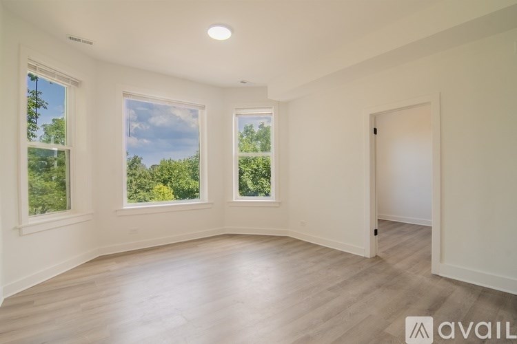 A spacious room with wooden floors and three windows showing a view of trees and sky.