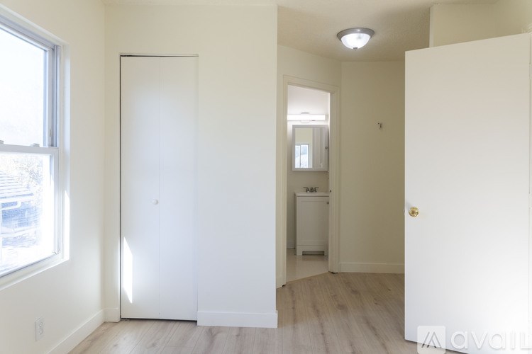 A white door is in a room with a window and a fridge.