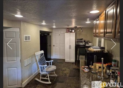 A kitchen with a white rocking chair and a black fridge.