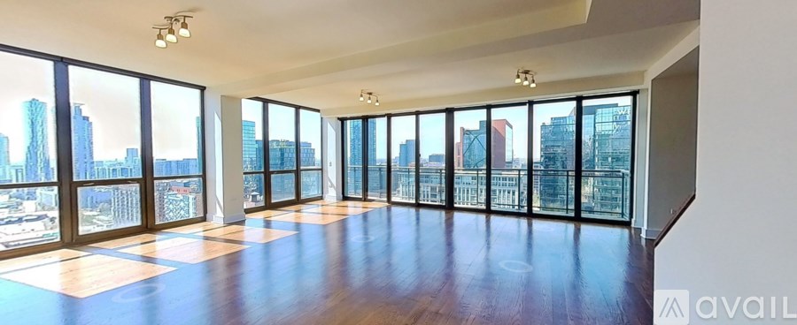 A large empty room with wooden floors and a view of the city through the windows.
