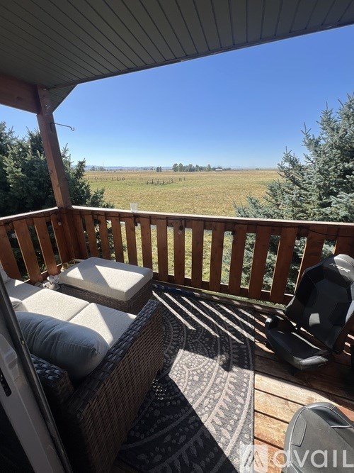 A balcony with a couch and a chair with a view of a field.