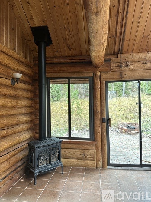 A wood stove is in a corner of a room with a window and a door.