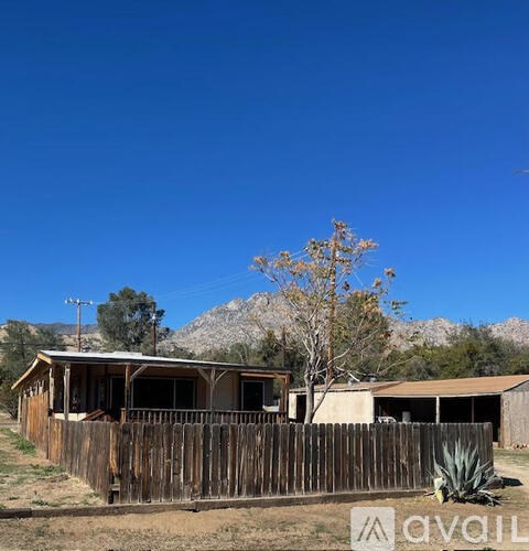 A wooden fence surrounds a house with a mountain in the background.