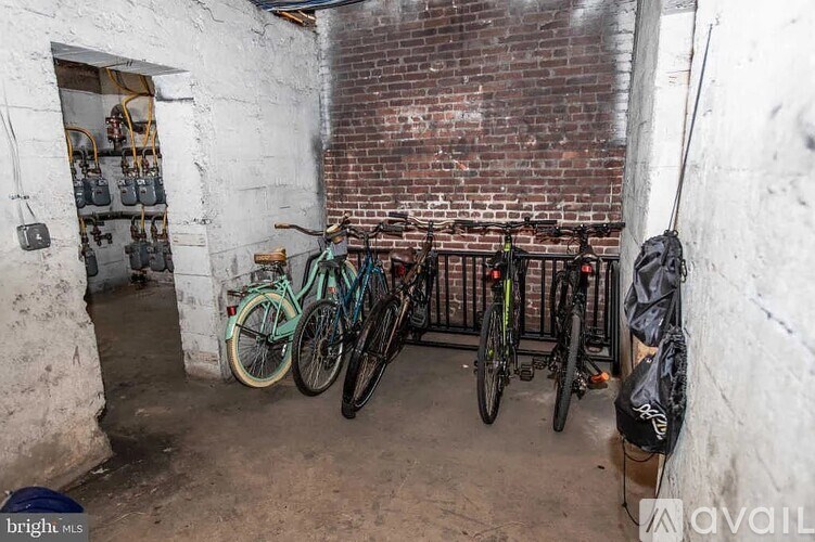 A room with a brick wall and a white door has several bicycles parked against it.