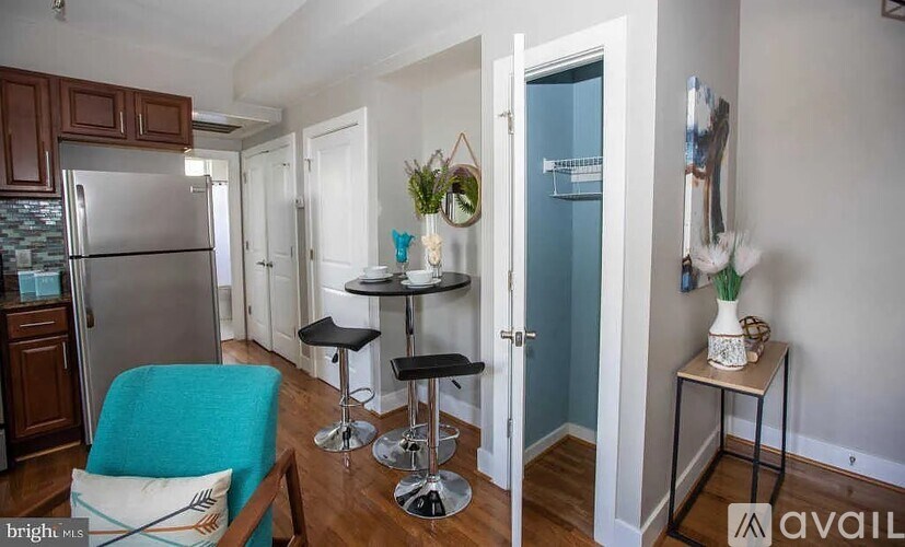A kitchen with a refrigerator, a table with two stools, and a blue chair.
