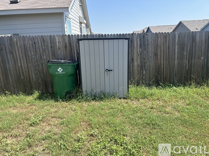 A green trash can sits next to a grey metal shed in a backyard.