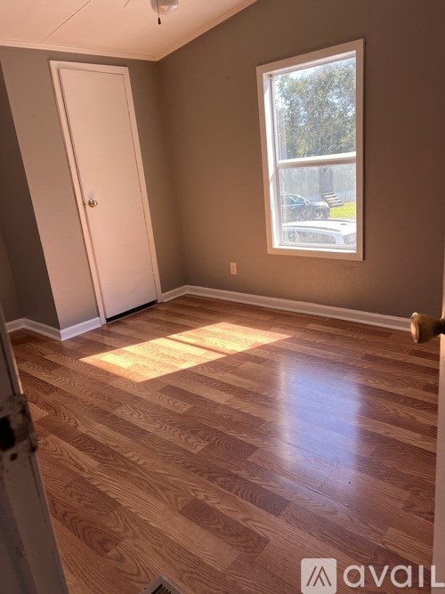A room with wooden flooring and a window showing a view of a parking lot.