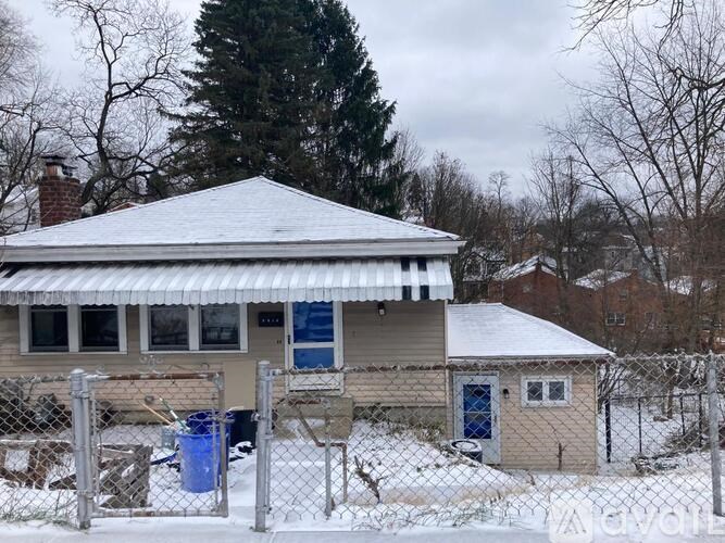 A house with a grey roof and a blue door is surrounded by a fence.