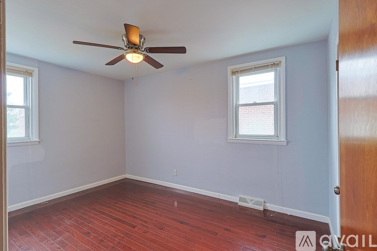 A room with a ceiling fan and two windows.
