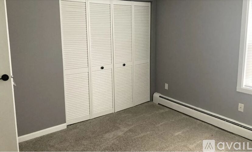A room with grey walls and a carpeted floor with three white closet doors.