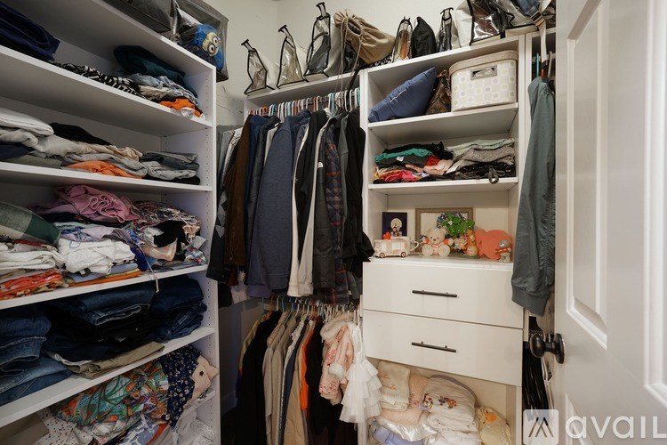 A white closet with clothes and drawers.