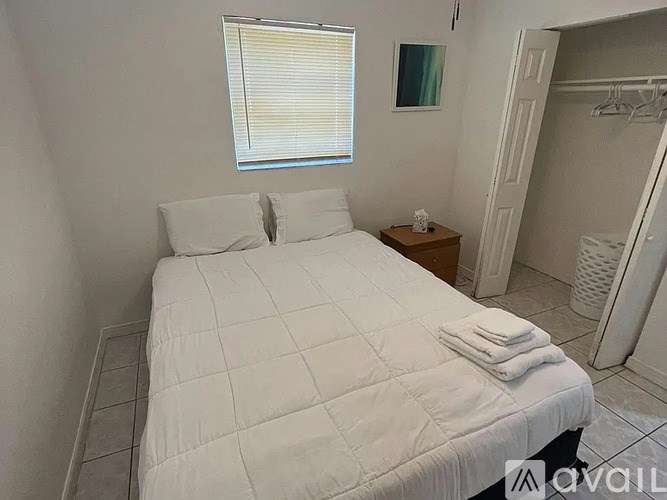 A white bed with a white comforter and pillows with a small wooden nightstand with a lamp and a picture frame on it.
