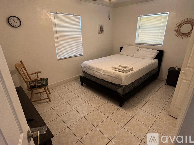 A bedroom with a bed, chair, and clock on the wall.
