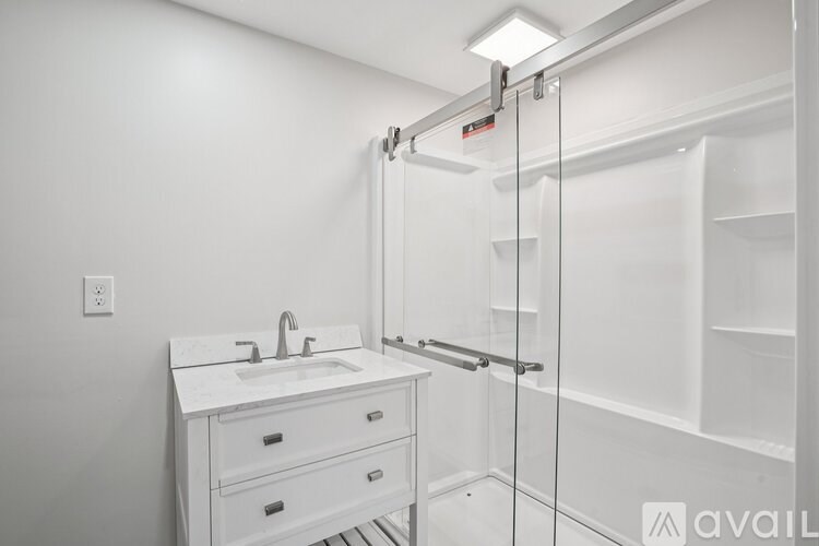 A white bathroom with a sink and a glass shower stall.