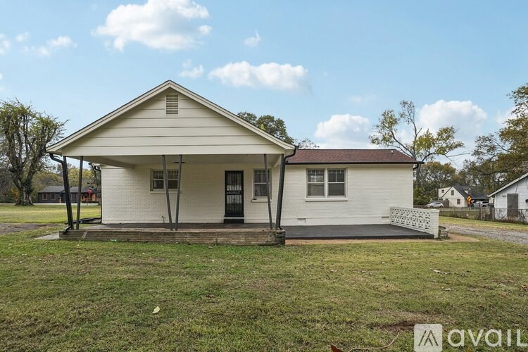 A white house with a porch and a brown roof is surrounded by a grassy area.