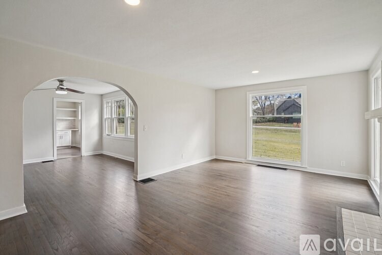 A spacious room with wood flooring and a large window overlooking a green field.