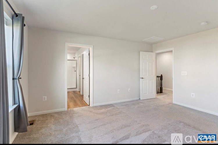 A spacious room with a carpeted floor and white walls, with a doorway leading to another room.