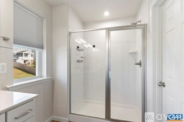 A white bathroom with a glass shower door and a window.