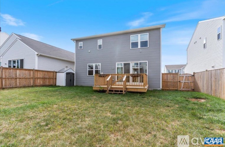 A grey house with a wooden deck in the front yard.