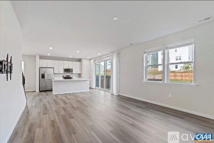 A spacious living room with wood flooring and a kitchen area in the background.