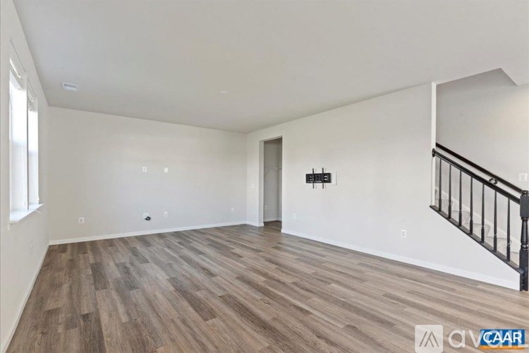 A spacious room with wooden flooring and a staircase on the right side.