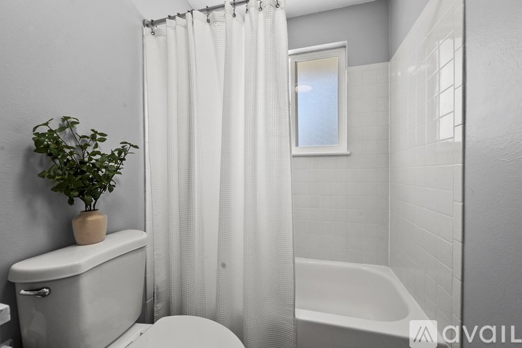 A white bathroom with a toilet, a bathtub, and a plant.