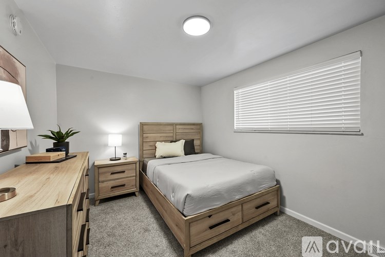 A bedroom with a bed, desk, and window with blinds.