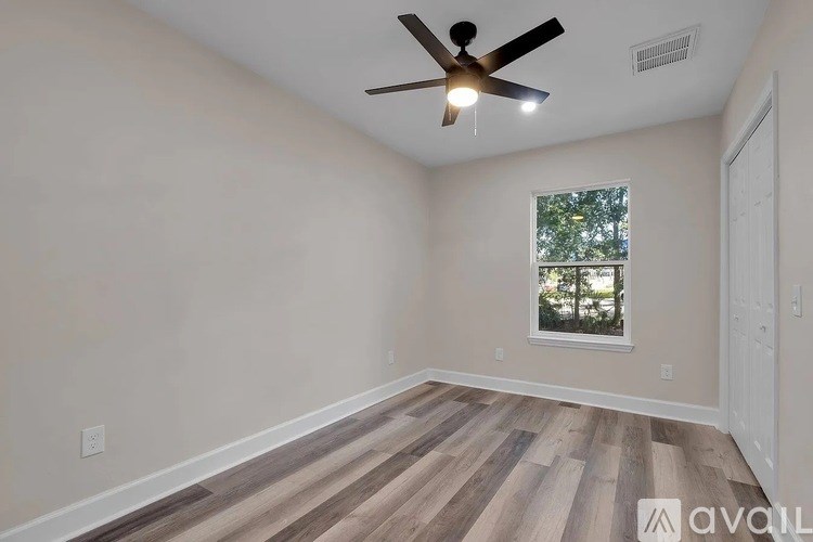 A room with a ceiling fan and a window with a view of trees.