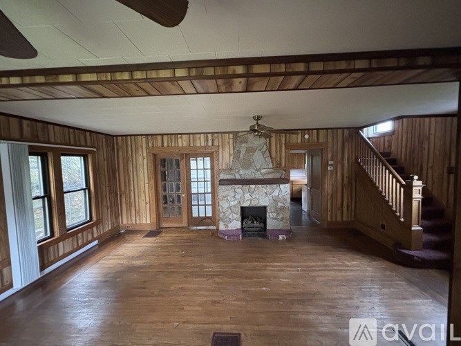 A large empty room with wood floors and a stone fireplace.