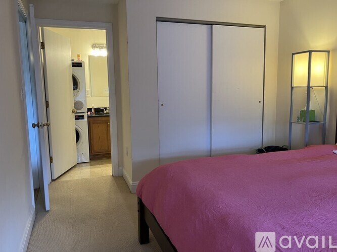 A bedroom with a pink bed and a lamp on a side table.