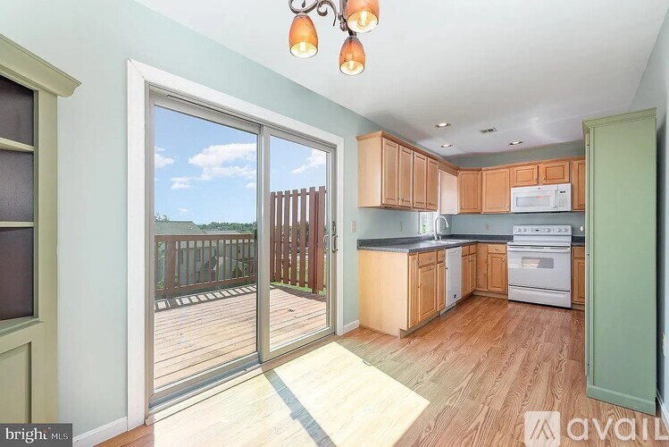 A brightly lit kitchen with wooden floors and a view of a deck outside through a sliding glass door.
