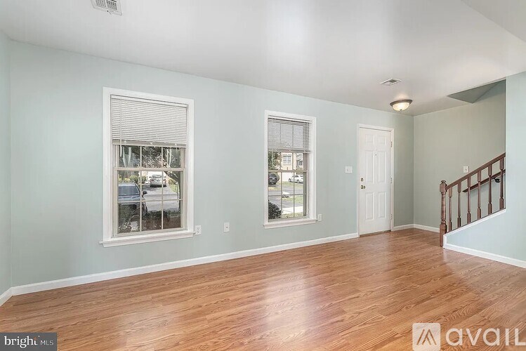 A room with wooden floors and two windows with blinds.