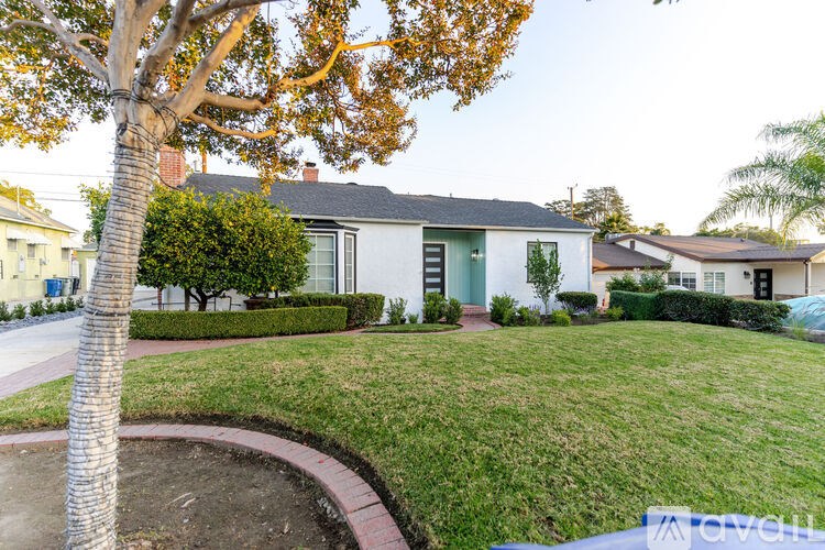A tree with yellow leaves is in front of a white house with a green door.