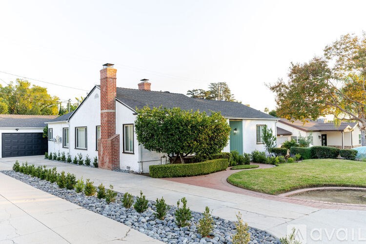 A white house with a brick chimney is surrounded by a gravel driveway and landscaping.