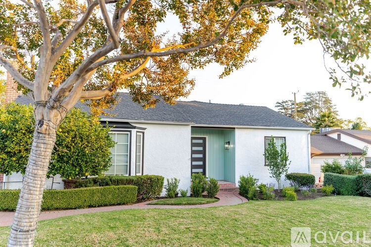 A white house with a green door is surrounded by a well-manicured lawn and trees.
