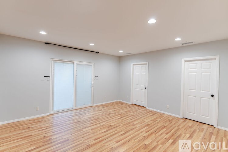 A room with wooden flooring and white walls, with three doors and recessed lighting.