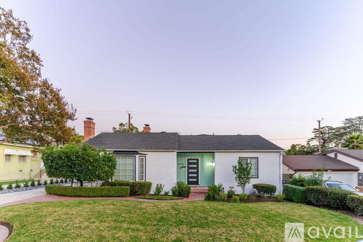 A house with a green door and a white exterior is surrounded by a well-kept lawn and trees.