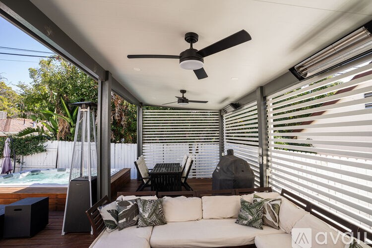 A modern outdoor living space with a white couch, a ceiling fan, and a hot tub.