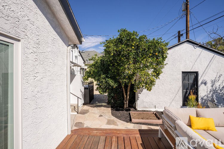 A white house with a wooden deck and a tree in front.