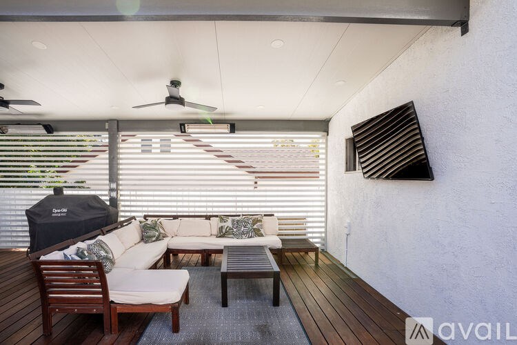 A patio with a white couch, wooden chairs, and a ceiling fan.