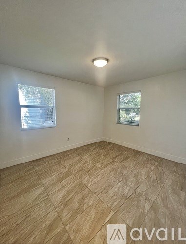 A room with wooden flooring and two windows.