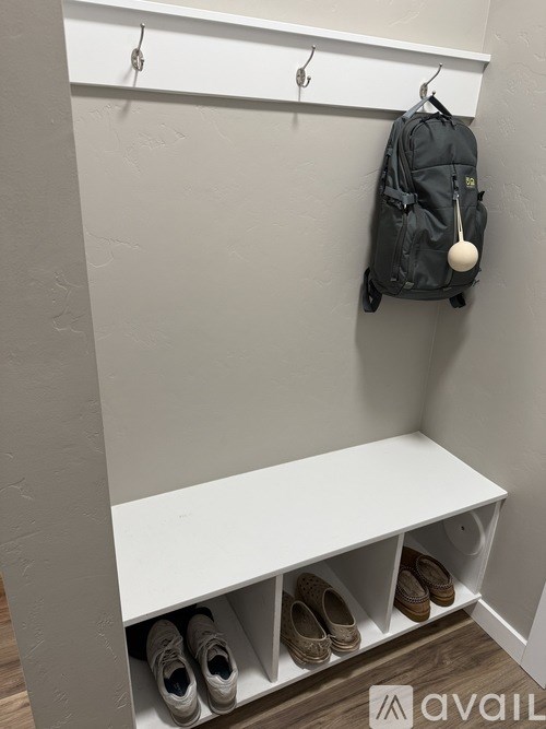 A black backpack is hanging on a hook in a white room.