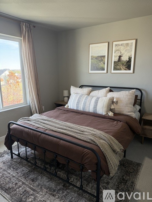 A bedroom with a bed, two pictures on the wall, and a window with curtains.