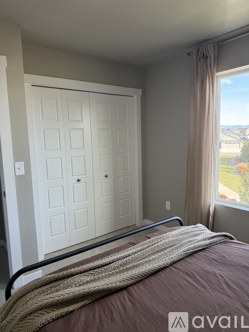 A bedroom with a bed, a window with a view of the outside, and a white door.
