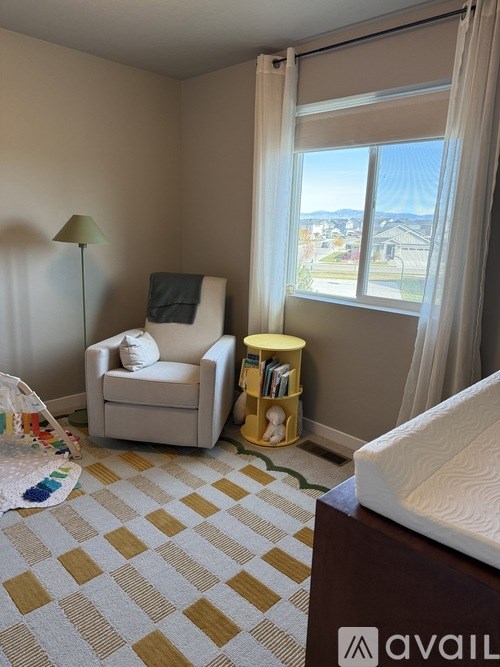 A room with a white chair, a lamp, a window with curtains, and a bed with a white mattress.