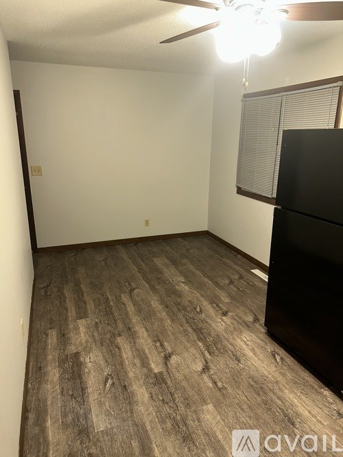 A room with a black refrigerator and wooden flooring.