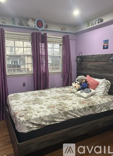 A bed with a floral bedspread sits in a room with purple walls and a window with purple curtains.